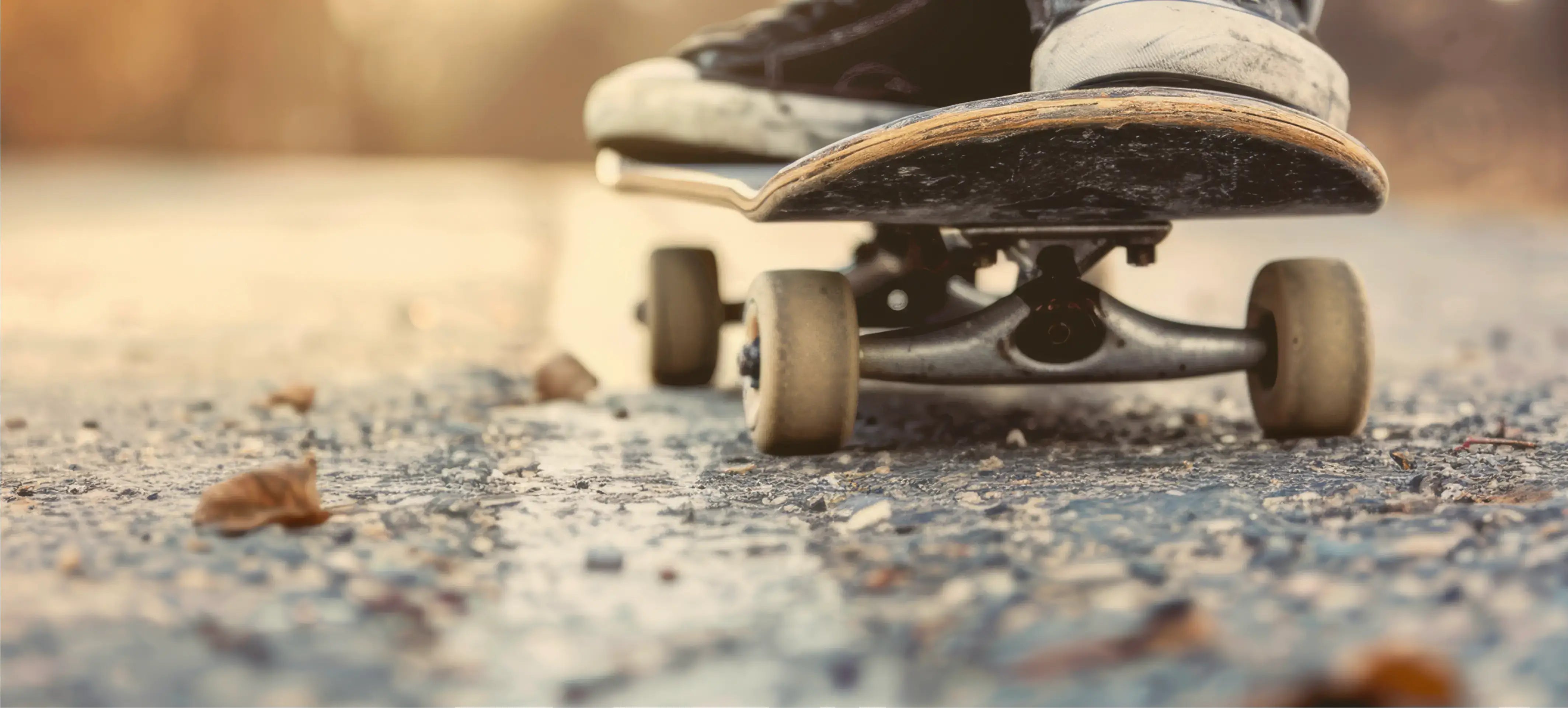 Nahaufnahme eines Skateboards auf einer Straße, mit einem Fuß auf dem Brett, umgeben von Laub.