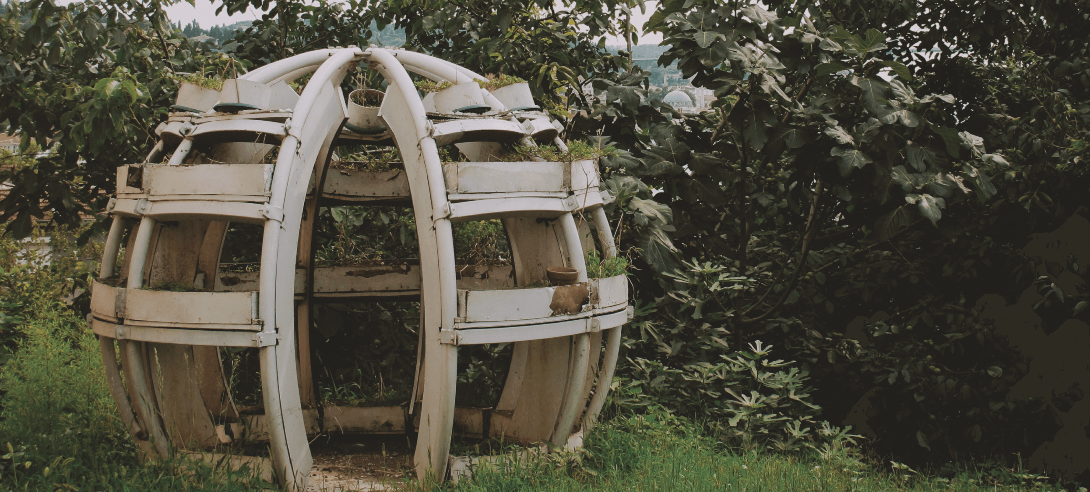 Verwitterter metallener Korpus inmitten von üppigem grünem Laub, die Struktur erinnert an eine futuristische Skulptur.