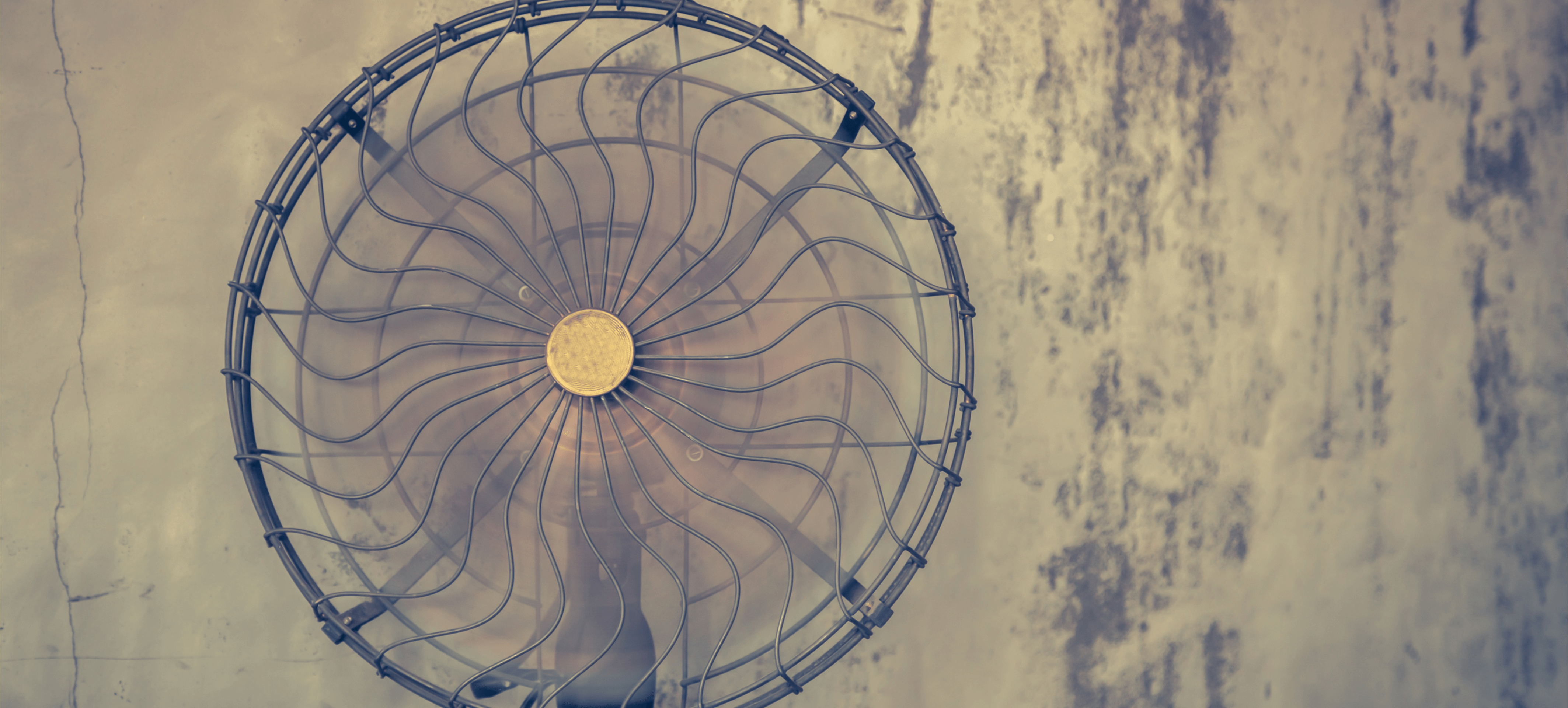 Alter Kühlventilator mit spiralförmigen Lamellen, angebracht an einer betagten Wand.