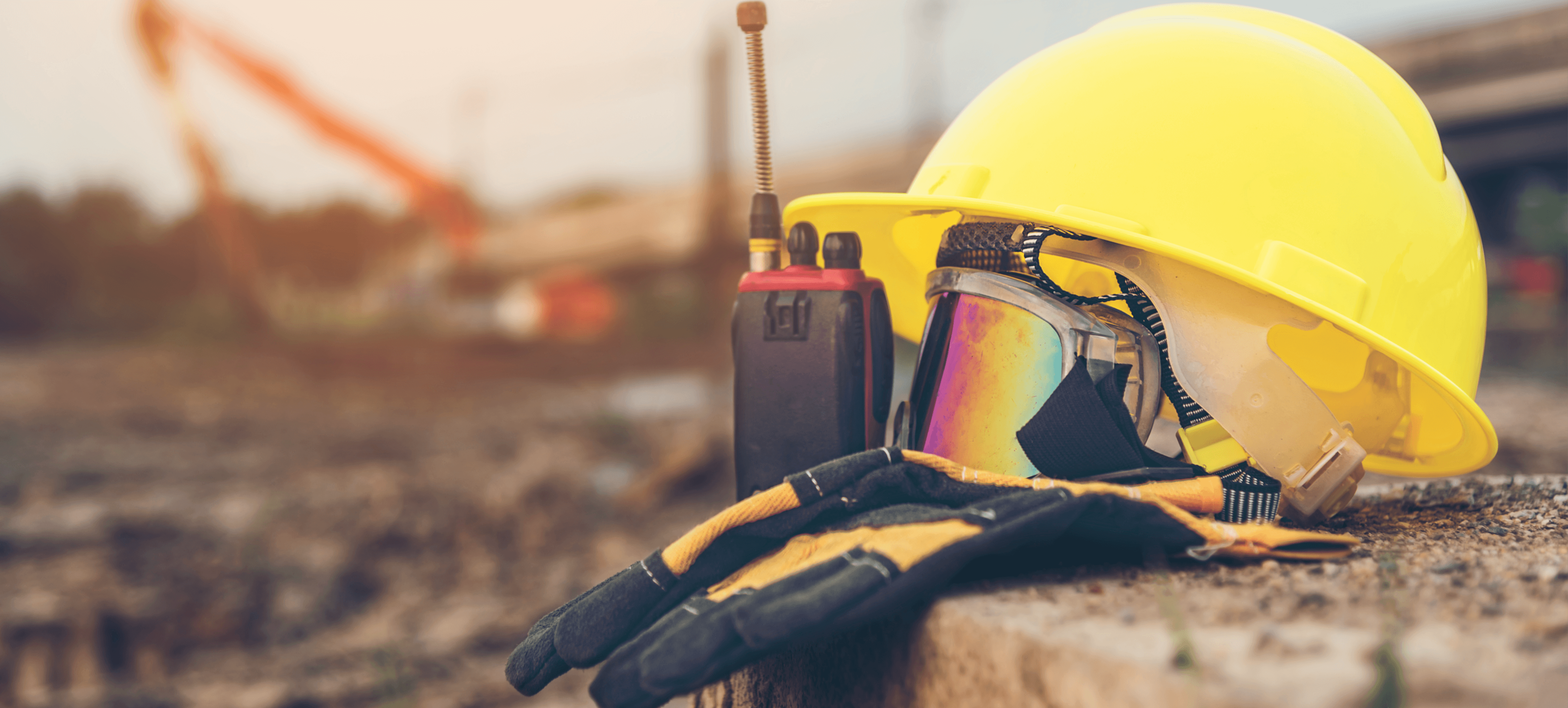 Safety equipment for construction: yellow hard hat, gloves, protective goggles, and a walkie-talkie.